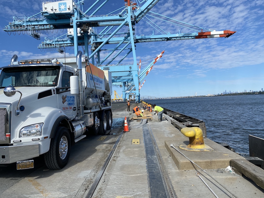 Crew pouring a concrete strip along a waterfront pier with the mixer truck alongside